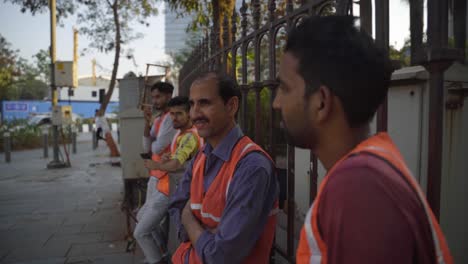 Portrait-of-a-group-of-Indian-male-construction-workers-in-safety-uniform-taking-evening-break-and-enjoying-the-roadside-view,-Bandra-Kurla-Complex,-Mumbai