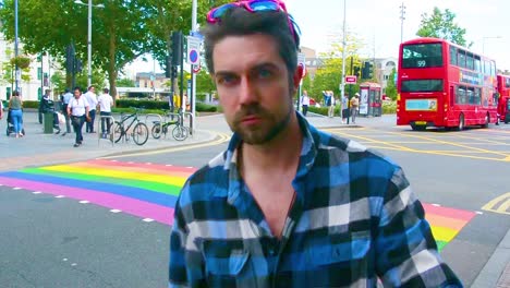 Handsome-man-getting-ready-for-gay-pride-with-pink-sunglasses-in-front-of-rainbow-pedestrian-crossing-in-London-for-pride-month,-eye-level-shot,-static-camera,-day,-real-time,-color-graded