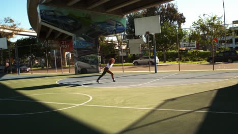 Slow-motion-wide-shot-across-urban-graffiti-basketball-court-watching-red-curly-haired-street-dancer-performing