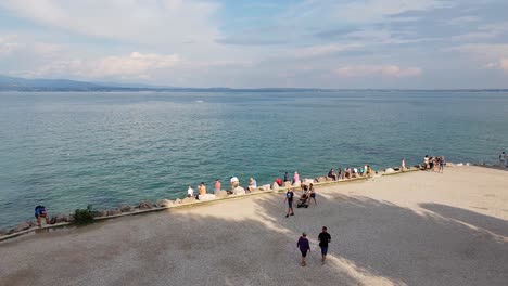 Tourists-enjoying-a-hot,-sunny-September-day-by-Sirmione-castle-in-Lake-Garda,-Northern-Italy