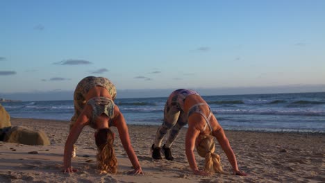 Zwei-Junge-Blonde-Mädchen-üben-Am-Sandstrand-Bei-Sonnenuntergang-Pilates-Yoga-Positionen-Aus