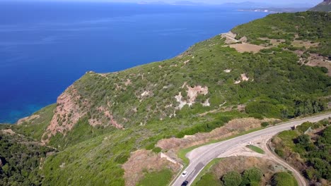Drone-aerial-shot-over-a-curvy-coastal-road-on-the-mediterranean-blue-sea,-while-cars-are-passing-by-the-road