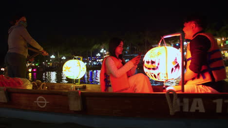 A-tracking-shot-of-tourists-riding-a-colorful-lantern-boat-along-the-river-in-the-city-of-Hoi-An,-Vietnam