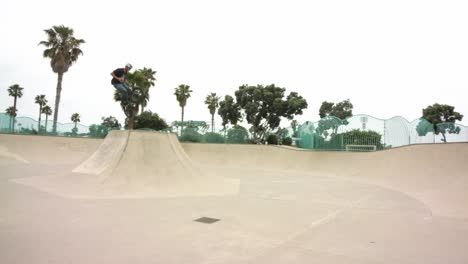 Wide-panning-shot-across-male-riding-bike-in-skate-park-jumping-ramps---performing-mid-air-tricks