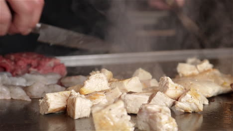 Der-Japanische-Koch-Schneidet-Hühnchen-In-Scheiben-Und-Kocht-Es-Auf-Einem-Flachen-Teppanyaki-Grill