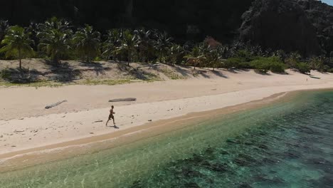 Aerial-slow-motion-drone-shot-of-a-man-exercising,-on-a-tropical-beach,-near-clear,-turquoise-water,-at-Black-island,-in-Philippines,-Asia