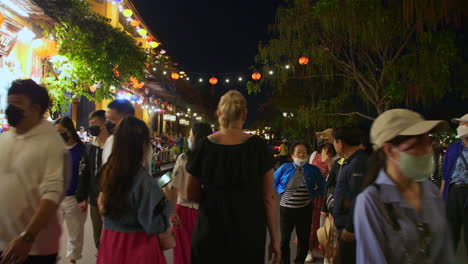 POV-shot-of-tourists-walking-tour-in-ancient-town-of-Hoi-An-decorated-with-colorful-lanterns-alongside-river-at-night,-Vietnam