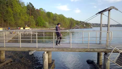 Side-Drone-Shot-of-a-tourist-walking-on-a-pier-at-Nordstrand-Bad-during-sunset-in-Oslo,-Norway