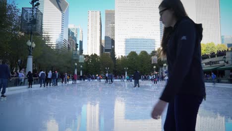 Ice-skating-people-at-McCormick-Tribune-Plaza-with-cityscape-on-the-background-in-Chicago,-IL