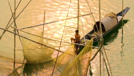 Young-fisherman-net-fishing-on-boat-in-river-at-dusk
