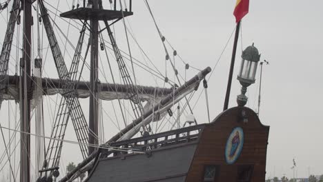 Galleon-Andalucia-replica-ship-detail-tilt-shot-of-spanish-flag,-pole-and-back-while-docked-in-Valencia-in-slow-motion-60fps