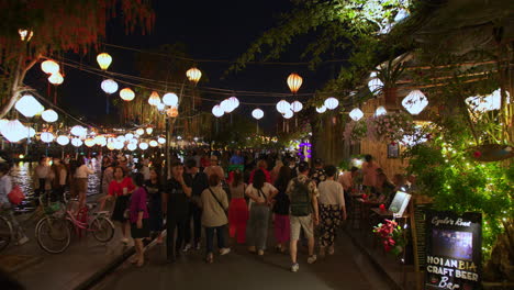 POV-shot-of-local-people-and-tourists-walking-tour-in-the-ancient-town-of-Hoi-An-decorated-with-colorful-lanterns-alongside-Hoai-River-at-night,-Vietnam