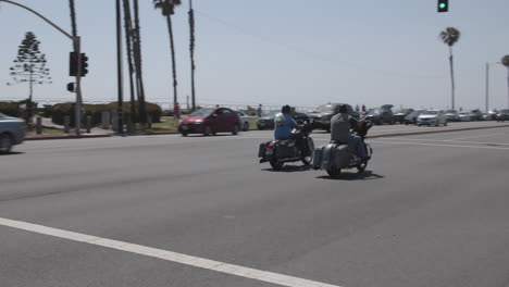 Men-driving-motorcycles-near-Long-Beach-pier-in-the-summer-with-palm-trees-and-beach-in-the-background