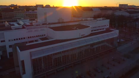 Helsinki-opera-house,-aerial,-rising,-drone-shot,-tilting-down-towards-Suomen-Kansallisooppera,-at-sunset,-on-a-sunny,-spring-evening,-in-Helsingfors,-Uusimaa,-Finland