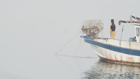 Pequeño-Barco-De-Pescadores-Recogiendo-Redes-De-Pesca-Con-Dos-Trabajadores-En-Mar-Tranquilo-Al-Amanecer-En-Cámara-Lenta-60fps