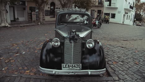 Classic,-vintage-car-parked-on-Uruguay-street-in-Costa-Colonia-with-motorcycles-driving-by-in-slow-motion
