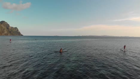 Aerial-drone-shot-over-people-sup-paddleboarding,-in-a-shallow,-turquoise-sea,-at-a-beautiful,-tropical-isle,-the-Coron-island,-in-Philippines,-Asia