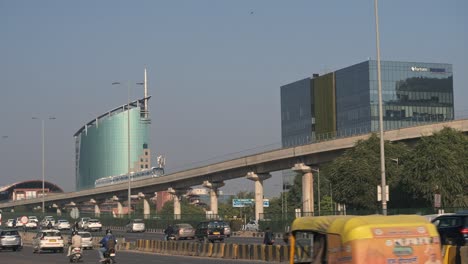 Wide-shot-of-modern-India-DLF-cybercity-Rapid-Metro-crossing,-commercial-building-in-background-and-smooth-traffic-movement-in-multilane-road