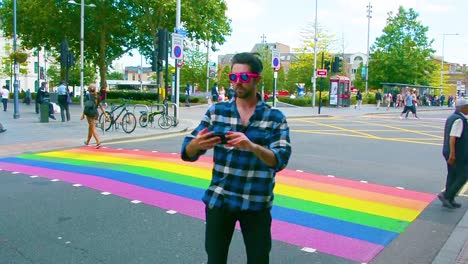 Handsome-man-taking-selfie-in-front-of-rainbow-pedestrian-crossing-in-London-for-pride-month,-eye-level-shot,-static-camera,-day,-real-time,-color-graded