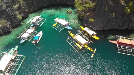 Aerial-drone-shot-of-people-at-Paraw-boats,-in-turquoise-lagoons,-between-limestone-cliffs,-on-a-sunny-day,-at-Coron-island,-Philippines,-Asia