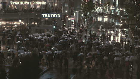 Multitudes-Caminando-Por-El-Cruce-De-Shibuya-Por-La-Noche-Con-Paraguas-Bajo-La-Lluvia,-Tokio,-Japón