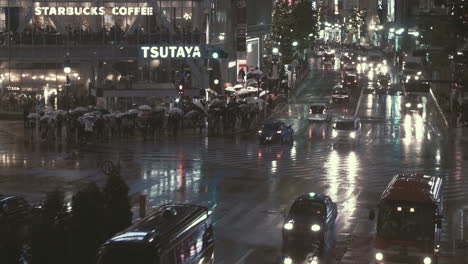 Tráfico-Por-Carretera-Pasando-Por-El-Cruce-De-Shibuya-Por-La-Noche,-Bajo-La-Lluvia,-Tokio,-Japón