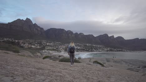 Blonde-Girl-is-walking-to-Camps-Bay-with-Table-Mountain-in-the-Background-in-Cape-Town,-South-Africa,-in-Slow-Motion