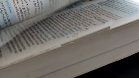 Close-up-slomo-panning-shot-of-an-Oxford-English-Dictionary,-a-male-hand-scrubs-through-it's-pages