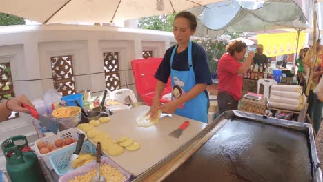 Thai-street-food---women-preparing-and-bakes-pancakes,-sweet-roti-with-bananas,-eggs-and-butter