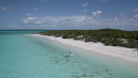 Bahamas-Tourist-Paddleboarding-to-Tropical-White-Sand-Beach,-Aerial-Drone