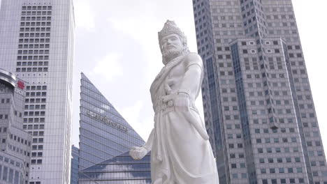 Statue-of-a-Palembang-Prince,-Sang-Nila-Utama-standing-tall-beside-the-Singapore-river-in-the-afternoon,-financial-office-buildings-in-the-background