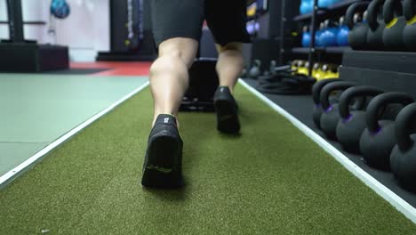 A-strong-man-is-pushing-a-prowler-sled-in-the-gym-on-the-green-turf-floor
