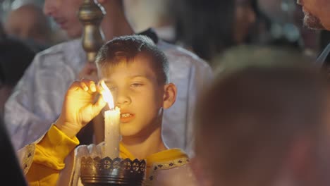 Young-boy-in-night-Easter-parade-robes-plays-with-his-burning-candle