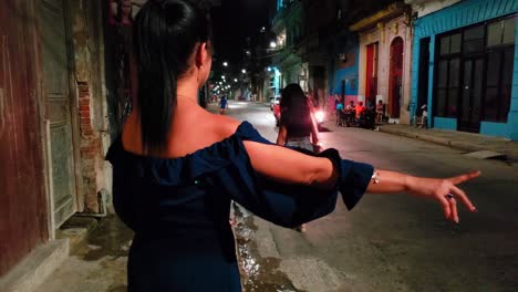 Cuban-woman-waiting-for-taxi-cab-at-night,-tourists-in-street,-Havana
