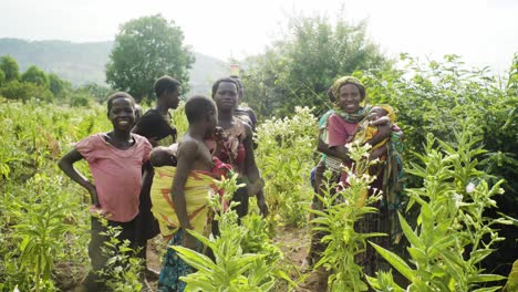 Portrait-of-a-curious-farmer-family-standing-in-a-field-of-crops-while-carrying-two-babies-in-rural-Uganda