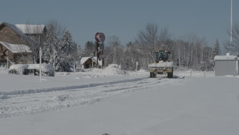 Yellow-tractor-clears-snow-from-a-road-on-a-sunny-winter-day