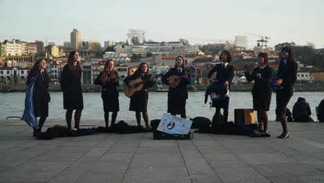 Vollständige-Zeitlupenaufnahme,-Eine-Gruppe-Junger-Studenten,-Die-Ihre-Instrumente-Spielen-Und-Singen,-Im-Hintergrund-Der-Fluss-Douro