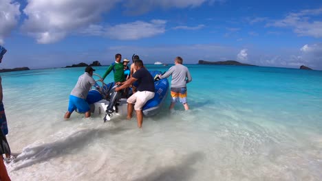On-a-white-sand-and-turquoise-water-beach-of-the-Galapagos-islands-several-tourists-are-getting-on-the-boat-while-two-men-are-holding-the-boat-steady