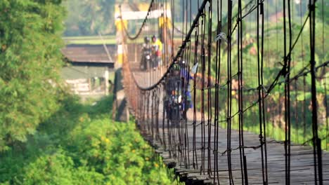 Menschen-Fahren-Mit-Dem-Motorrad-über-Die-Hängebrücke,-Um-Zur-Arbeit-Zu-Gehen-–-Ländliche-Aktivität-In-Der-Morgendlichen-Indonesischen-Landschaft