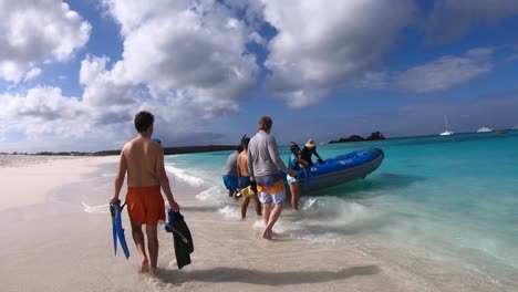A-group-of-tourists-is-getting-ready-to-board-a-small-blue-boat-on-a-paradisiac-beach-with-white-sand-and-turquoise-water-of-the-Galapagos-islands