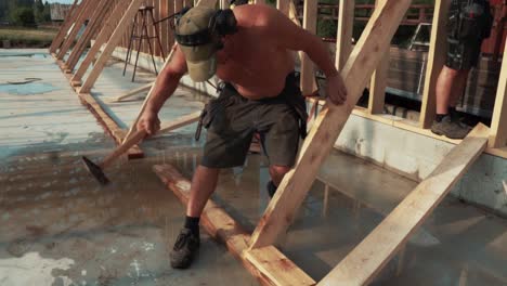 Adult-Male-Shirtless-Carpenter-Using-Hammer-On-Wooden-Beam-On-Construction-Site