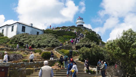 Lighthouse-on-top-of-a-hill-in-Cape-Point,-Cape-Town,-South-Africa-with-people-walking-up-the-steps