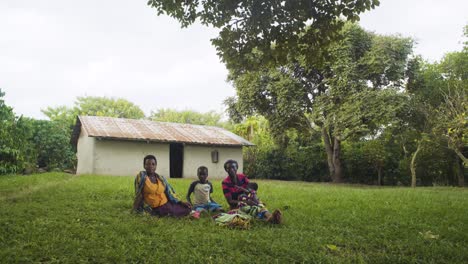 Porträt-Einer-Ugandischen-Bauernfamilie,-Die-Im-Gras-Ihres-Gartens-Sitzt,-Während-Der-Wind-Sanft-Durch-Die-Bäume-Weht