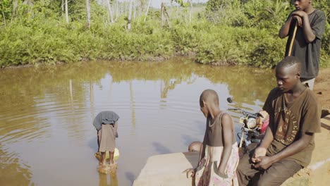 Drei-Kinder-Beobachten-Ihre-Mutter-Beim-Wasserholen-Aus-Einer-Kontaminierten-Pfütze-Im-Ländlichen-Uganda