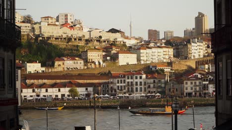 Einspielaufnahme,-Vorbeifahrendes-Segelboot-Auf-Dem-Fluss-Douro,-Malerischer-Blick-Auf-Die-Gebäude-Von-Porto-Und-Die-Menschen-Im-Hintergrund