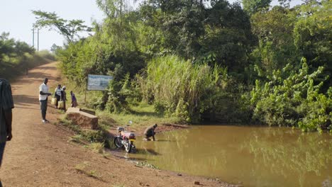 Dorfbewohner-Stehen-Um-Eine-Kontaminierte-Pfütze-Herum,-Während-Ein-Junge-Im-Ländlichen-Uganda-Wasser-Holt