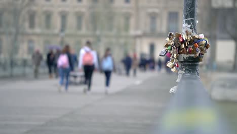 Clip-of-love-locks-on-a-pole-in-paris-city-centre-with-people-walking-in-the-background