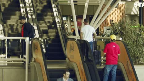 Travelers-with-luggage-riding-escalators-in-an-airport,-super-slow-motion