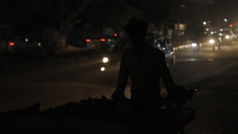 New-Delhi-India,-man-pushing-cart-on-busy-road-at-night