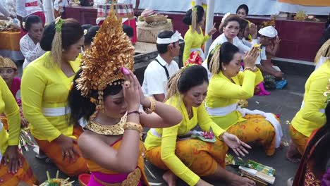 Una-Niña-Balinesa-Reza-Uniendo-Sus-Manos-En-Una-Ceremonia-Hindú-En-Bali-Vistiendo-Trajes-Tradicionales-Con-Joyas-Alrededor-De-Hermosas-Mujeres-Asiáticas